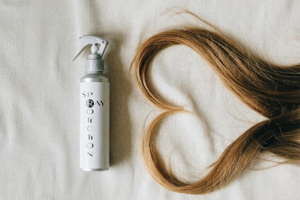Flat lay of hair spray bottle and heart-shaped hair on fabric background.