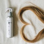 Flat lay of hair spray bottle and heart-shaped hair on fabric background.