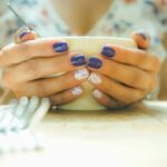 A woman with colorful nails holds a mug, capturing a moment of warmth and style indoors.