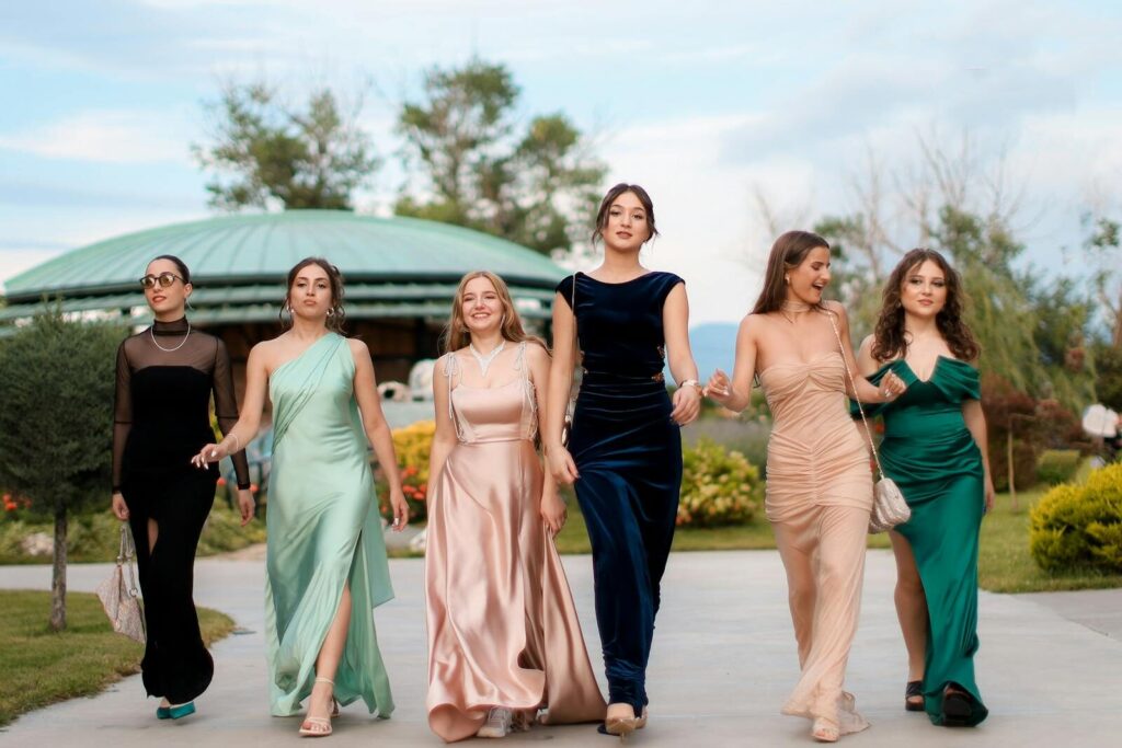 A group of six women in elegant evening dresses walking confidently outdoors, showcasing fashion and style.