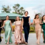 A group of six women in elegant evening dresses walking confidently outdoors, showcasing fashion and style.