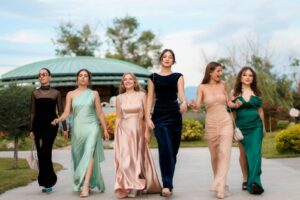 A group of six women in elegant evening dresses walking confidently outdoors, showcasing fashion and style.