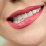 Close-up shot of woman's mouth wearing red lipstick, highlighting bright teeth and smooth skin.